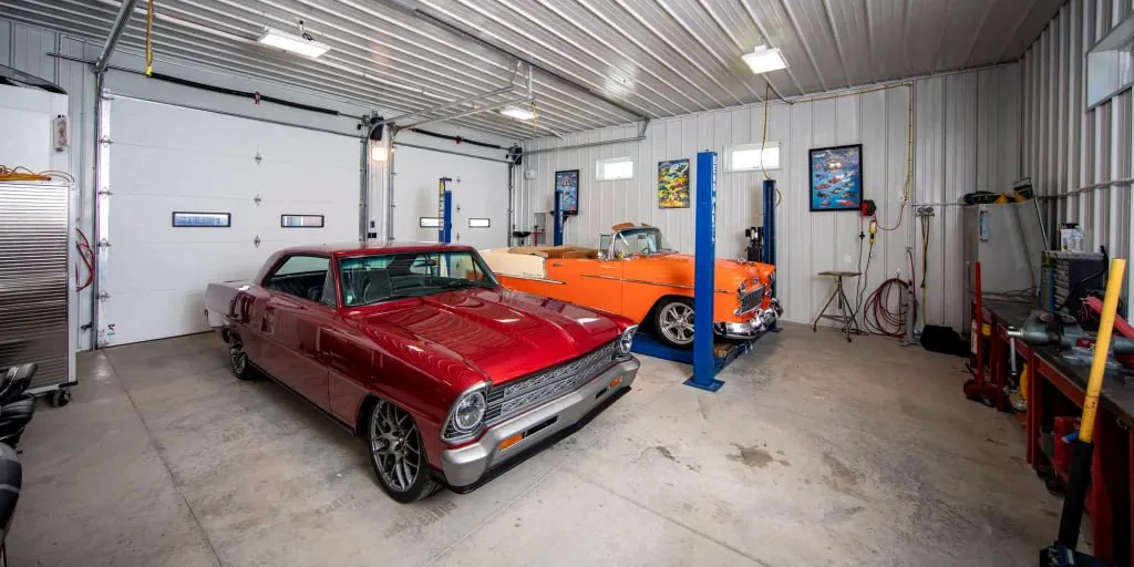 A red Chevy II Nova and an orange classic Chevy convertible on a lift inside a garage